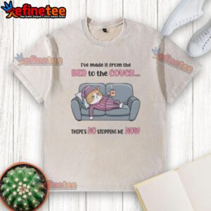 Alt Text: Tired cat wearing a washed t-shirt lounging on the couch after making the leap from the bed, looking relaxed.